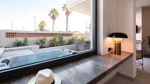 A modern bathroom with a large window, a bathtub, a shower area, and a vanity with a lamp.