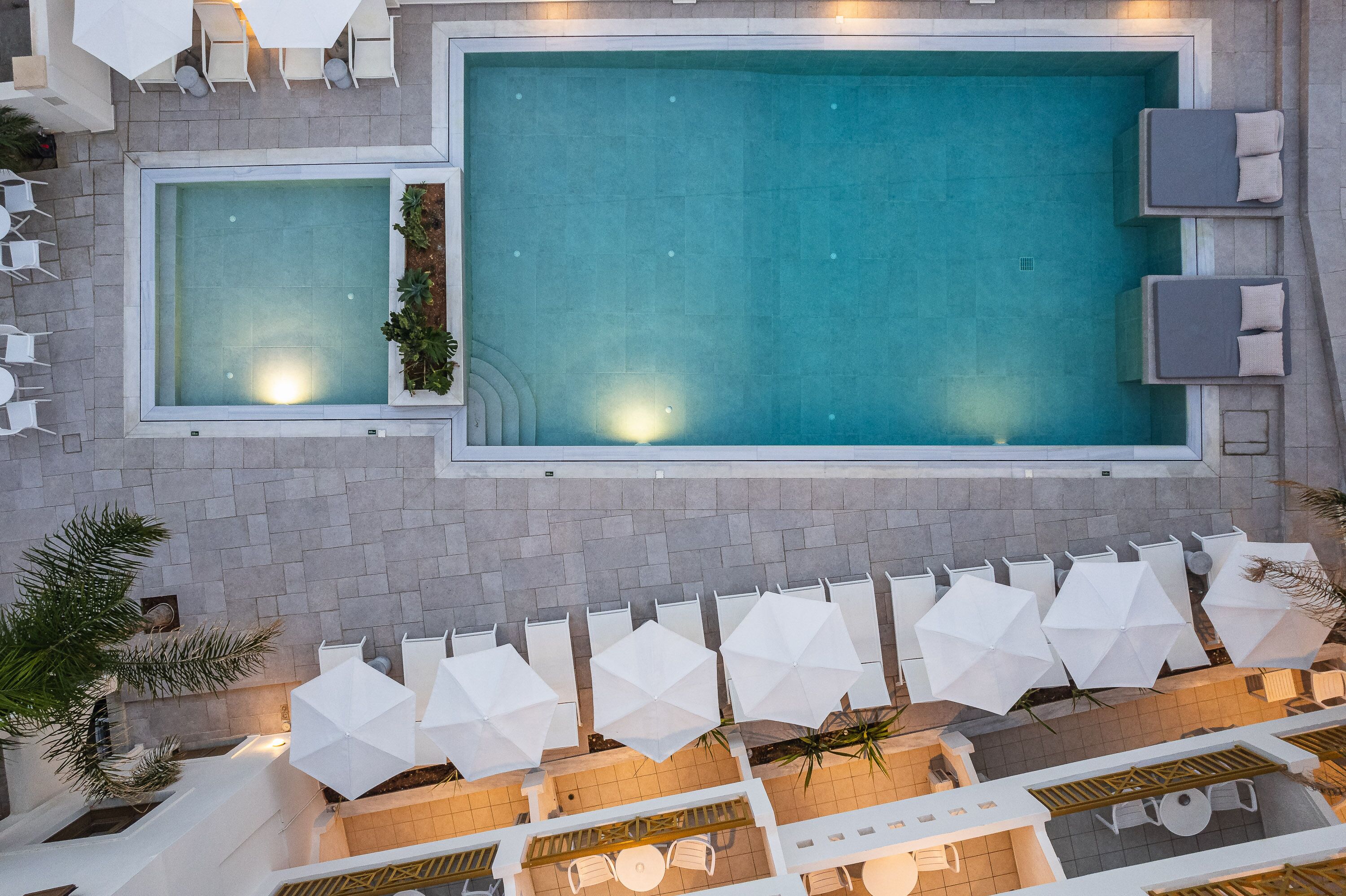 Un espace piscine sur le toit, comprenant deux piscines distinctes, des chaises longues, des parasols et un coin salon avec des tables.