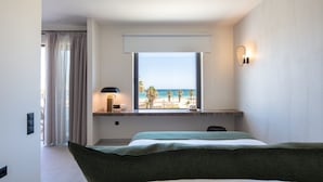A hotel room with a bed, a desk with a lamp, a view of the beach, and a window with curtains.