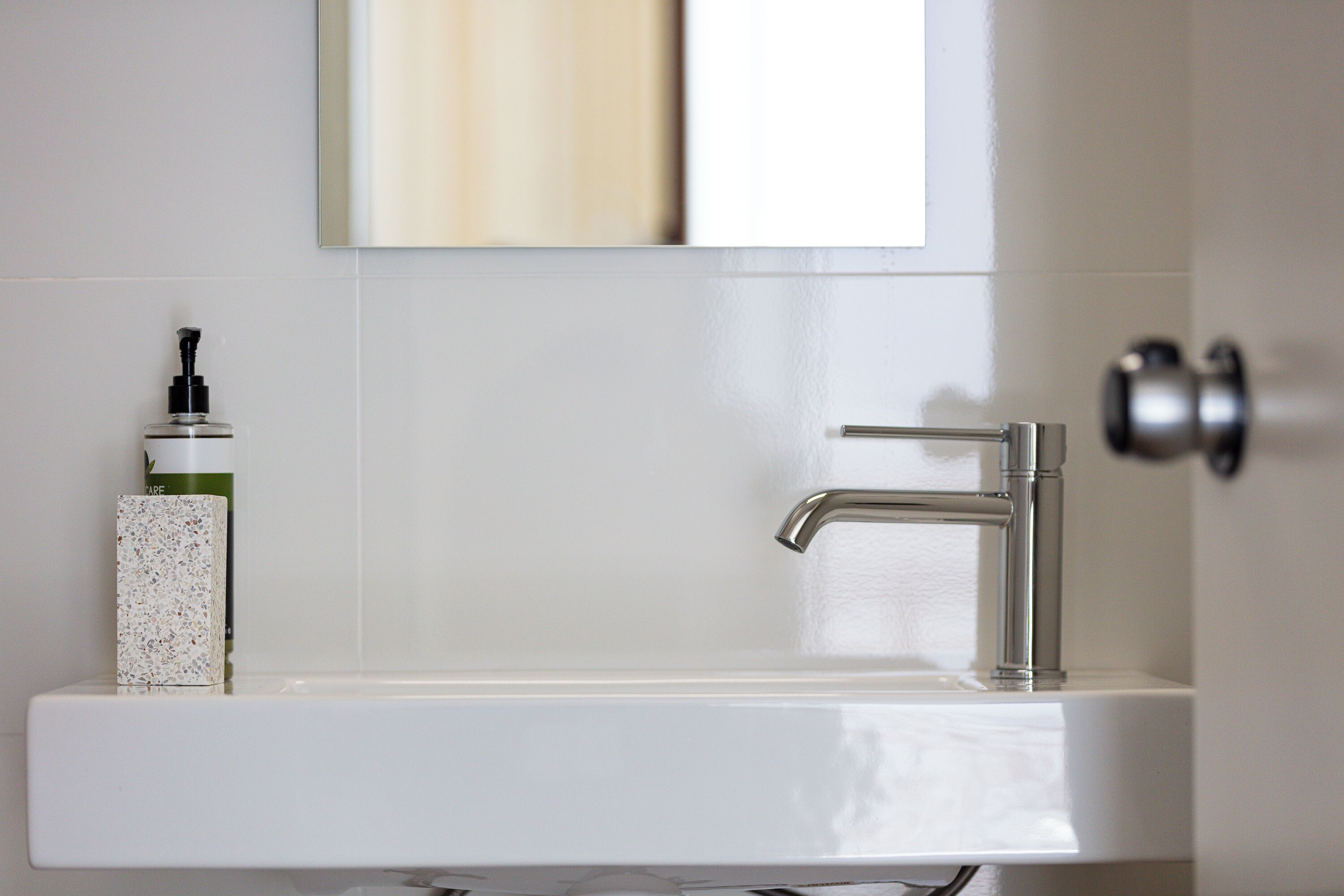 A bathroom with a white sink, a modern faucet, and a soap dispenser on the counter.