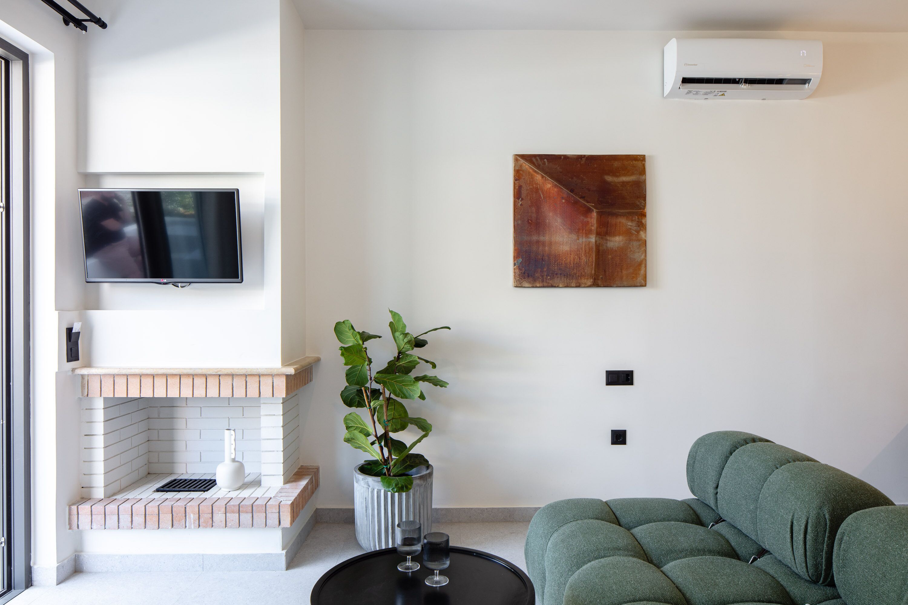 A modern living room with a flat-screen TV, a fireplace, a green sofa, and a potted plant.
