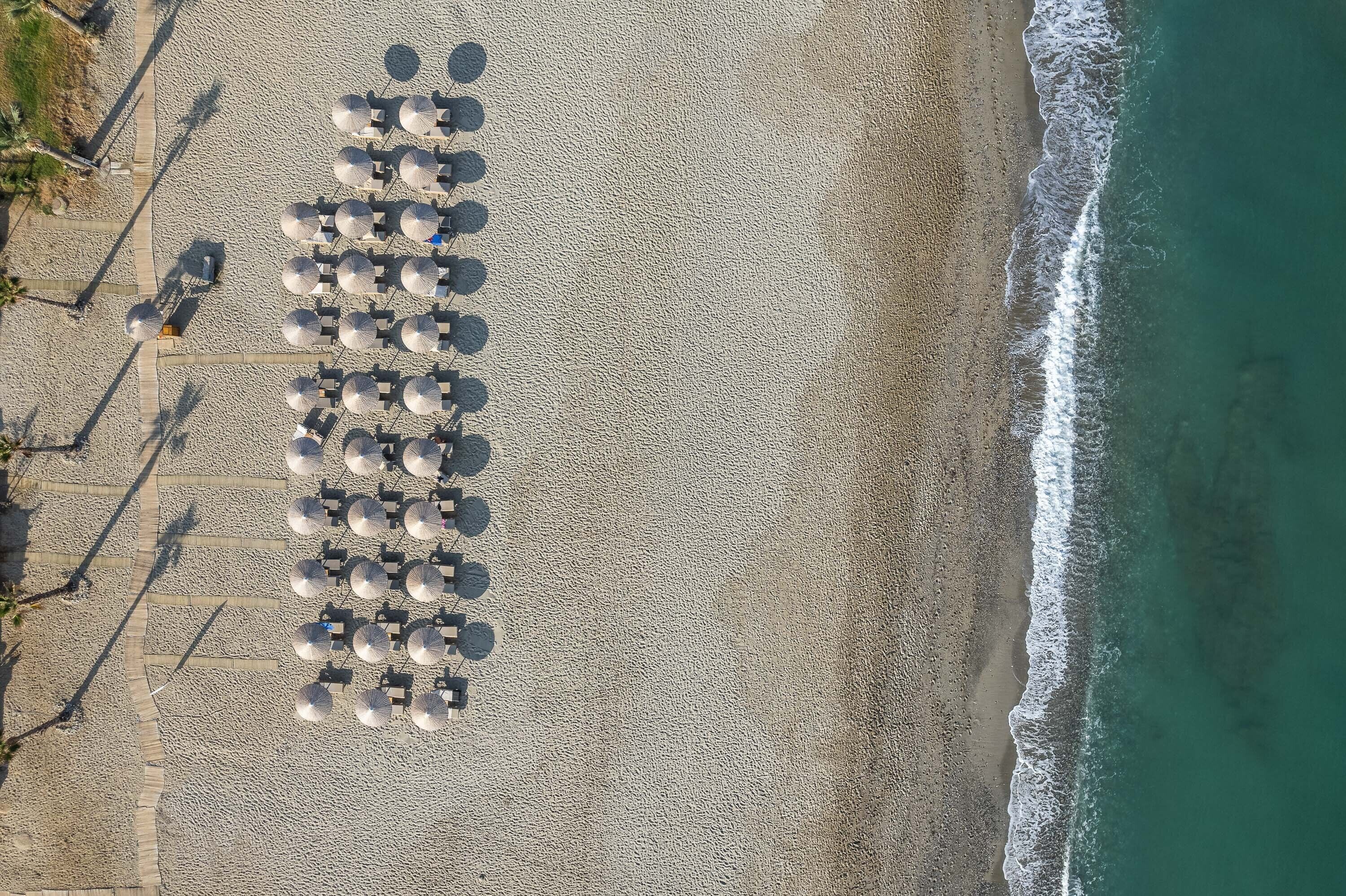 Vista aérea de una playa con hileras de sombrillas y tumbonas dispuestas para tomar el sol.