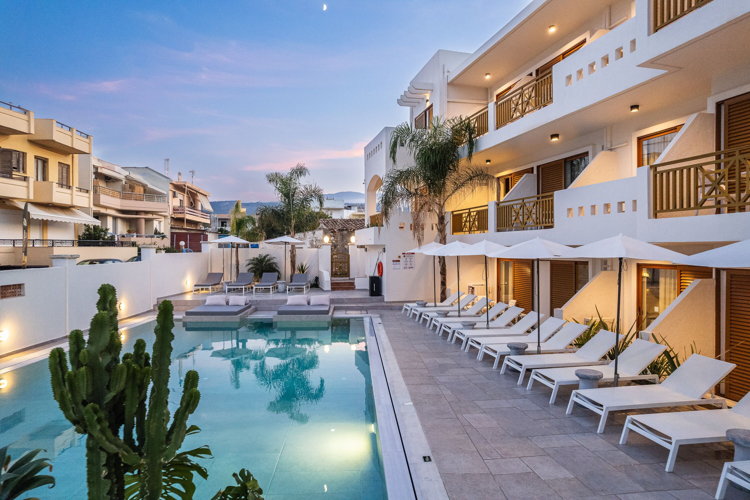 A poolside area with lounge chairs and umbrellas, a pool, and a building with multiple balconies and a modern design.