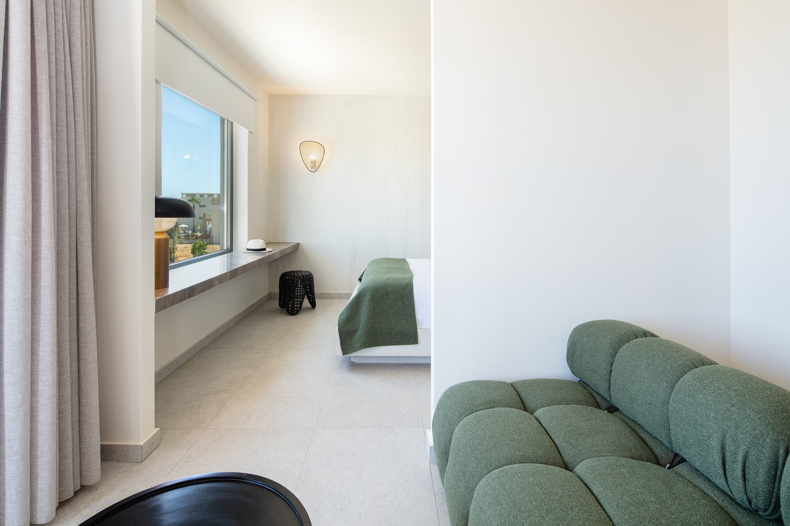 A bedroom with a bed, a window, a small stool, and a wall-mounted light fixture.