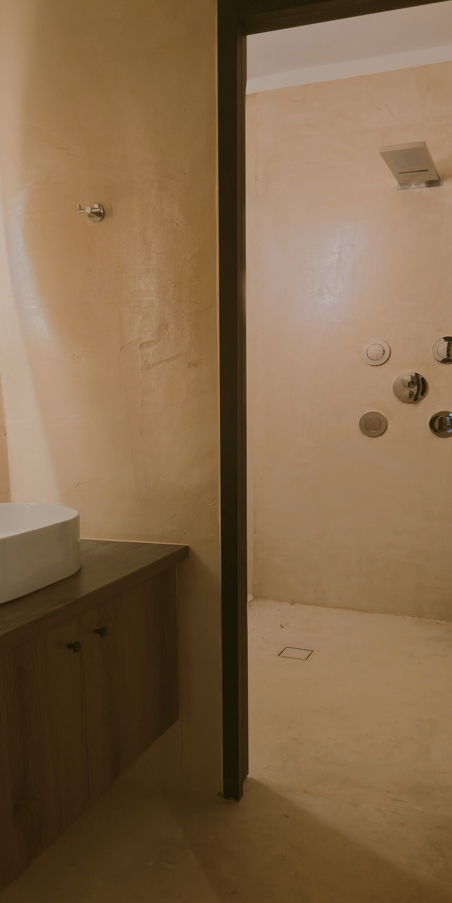 A bathroom with a beige wall, a wooden vanity with a sink, and a shower area with a ceiling-mounted showerhead.