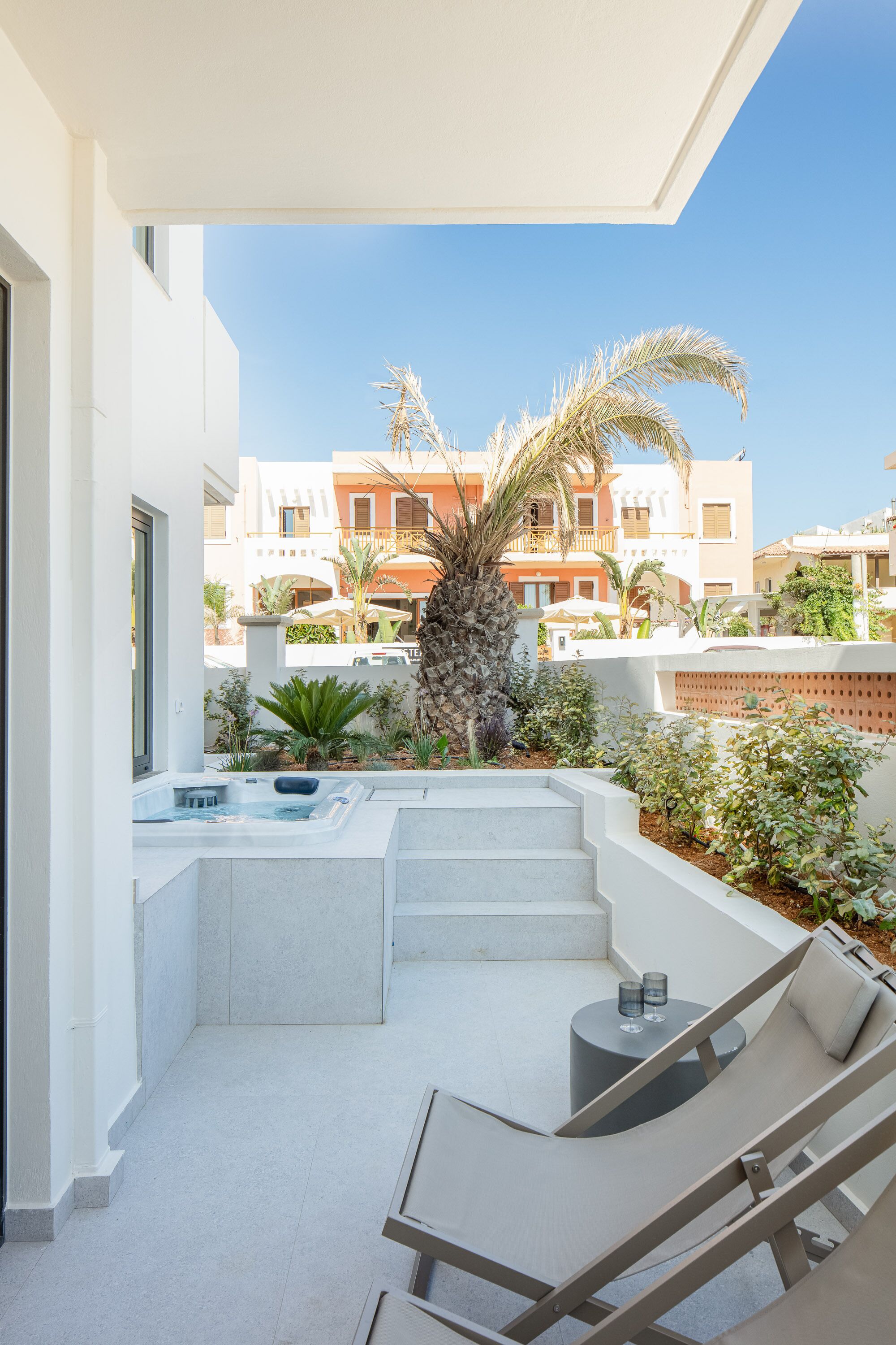 A modern outdoor patio with a hot tub, lounge chairs, and a view of a residential area.