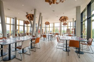 Un vaste espace dédié à la salle à manger, doté de hauts plafonds et de grandes fenêtres, et aménagé avec des tables et des chaises au design moderne.
