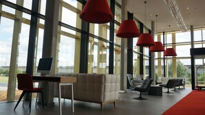 A modern interior with large windows, a sofa, chairs, and red pendant lights. - Martin's Red (Tubize)