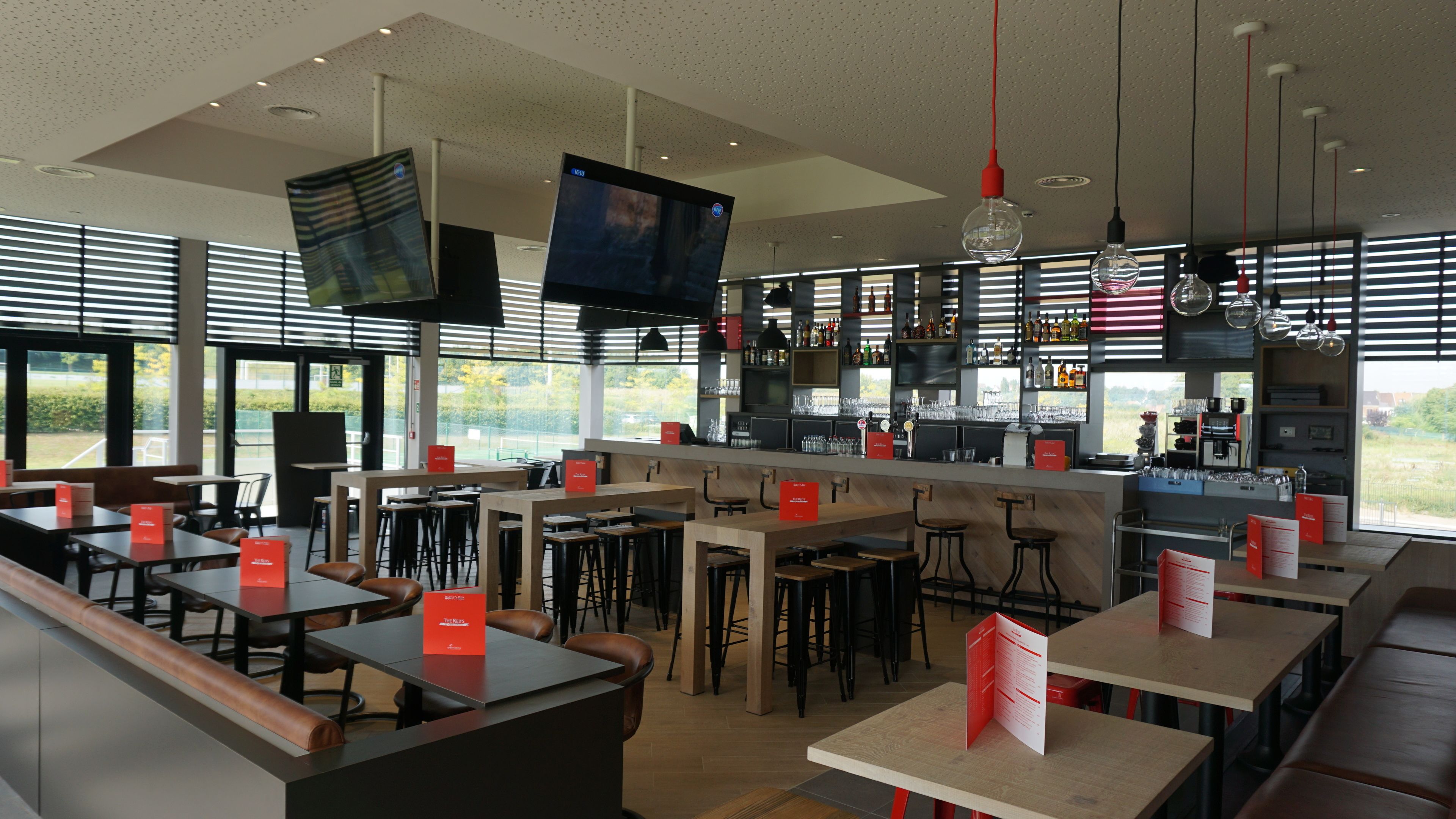Un restaurant moderne doté d’un bar, de plusieurs types de sièges, notamment des banquettes et des tables, et d’une grande fenêtre offrant une vue sur l’extérieur.