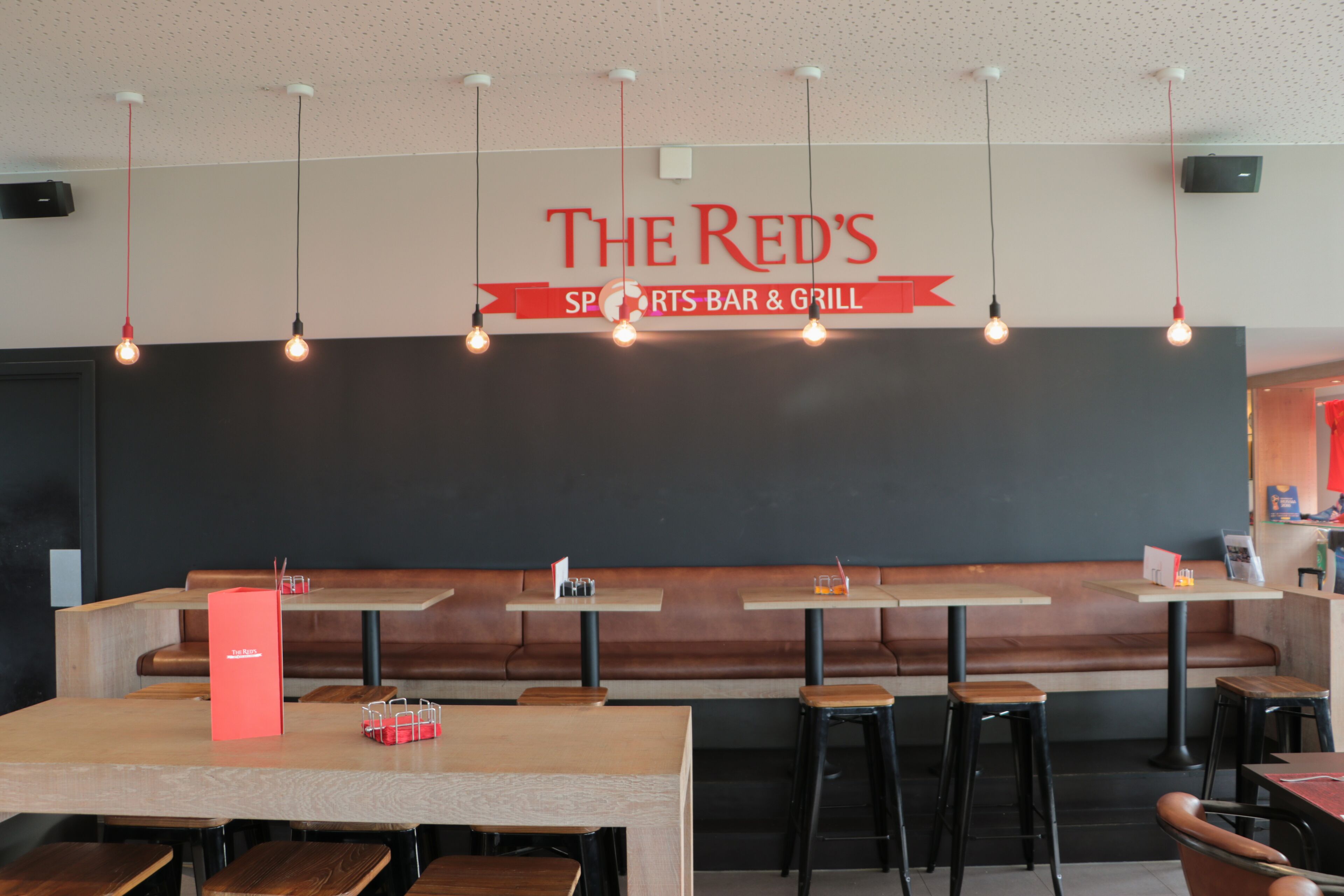 A sports bar and grill interior with wooden tables, black booths, and hanging pendant lights.