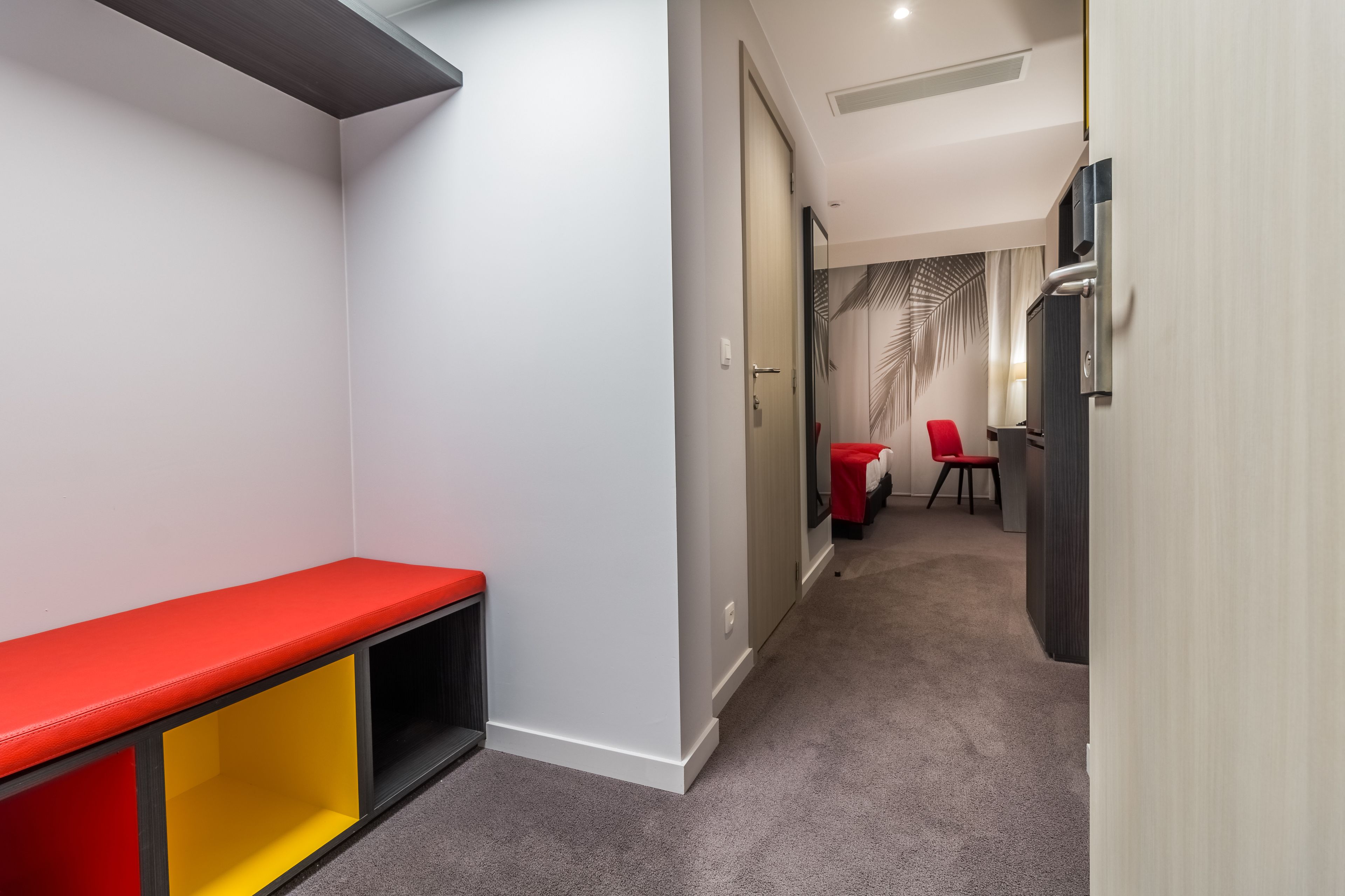 A hallway with a bench, a table with chairs, and a refrigerator.