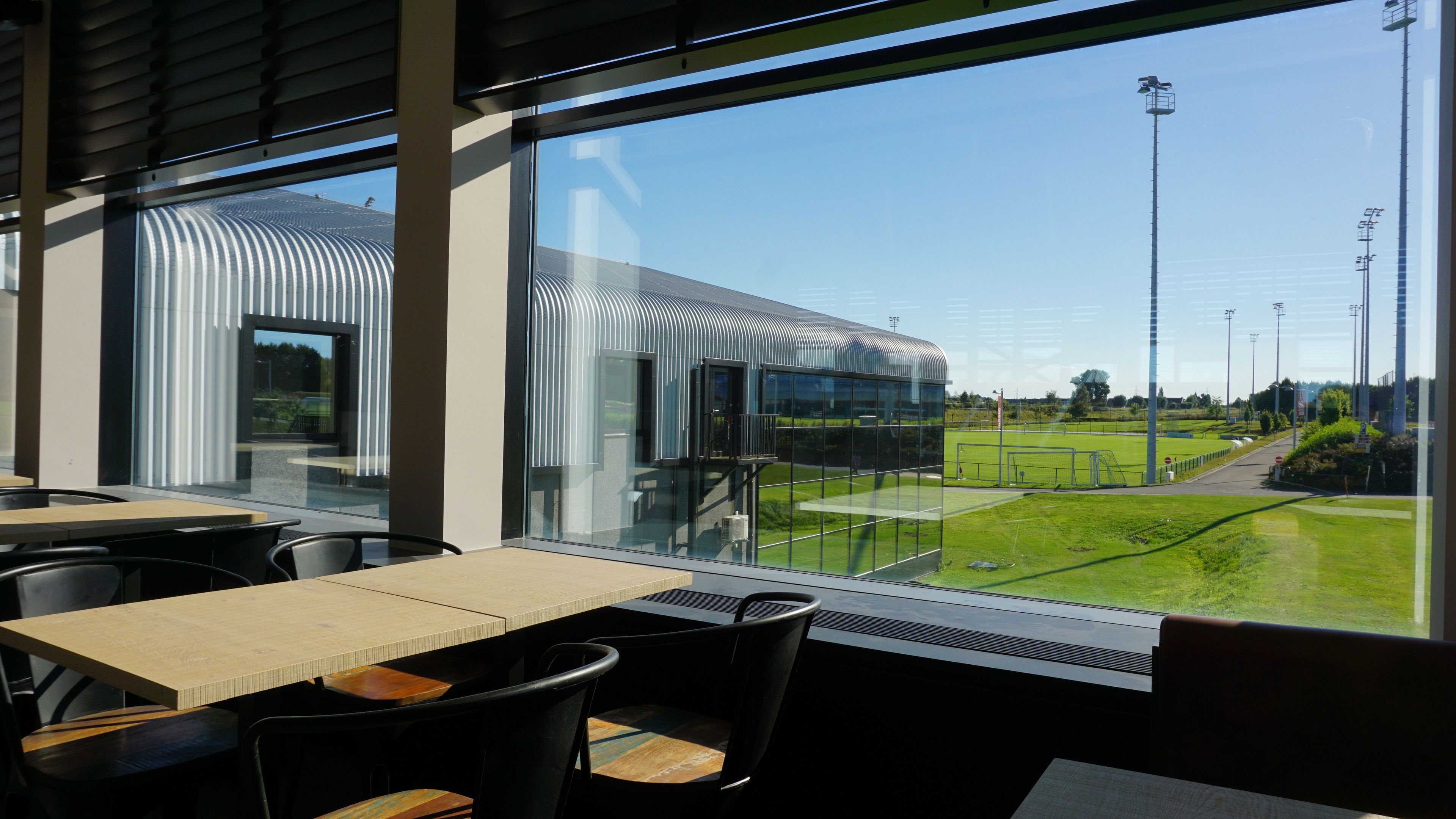 A modern restaurant with large windows offering views of a sports field and a building with a curved roof.