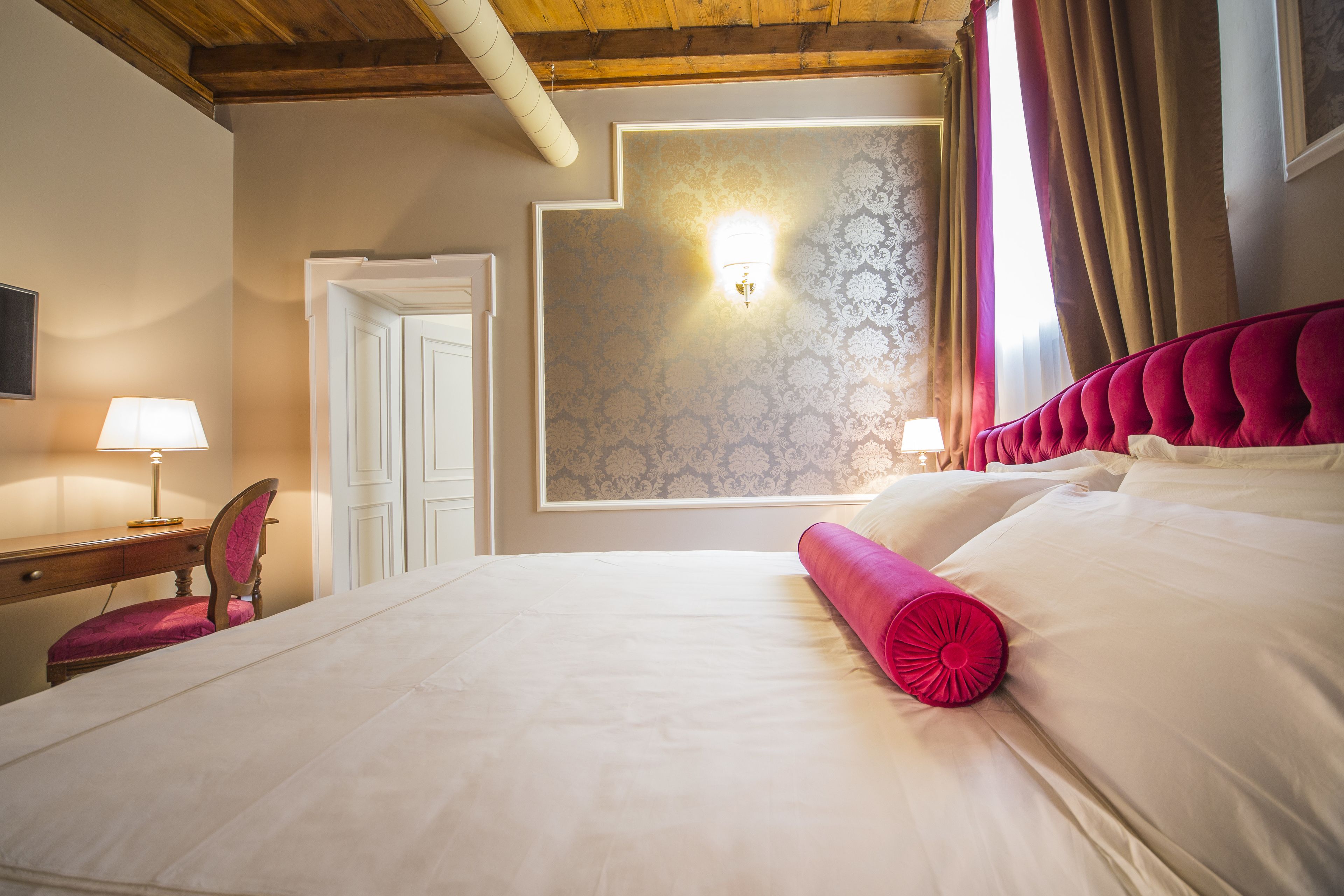 A hotel room with a large bed, a desk with a lamp, a chair, and a wardrobe.