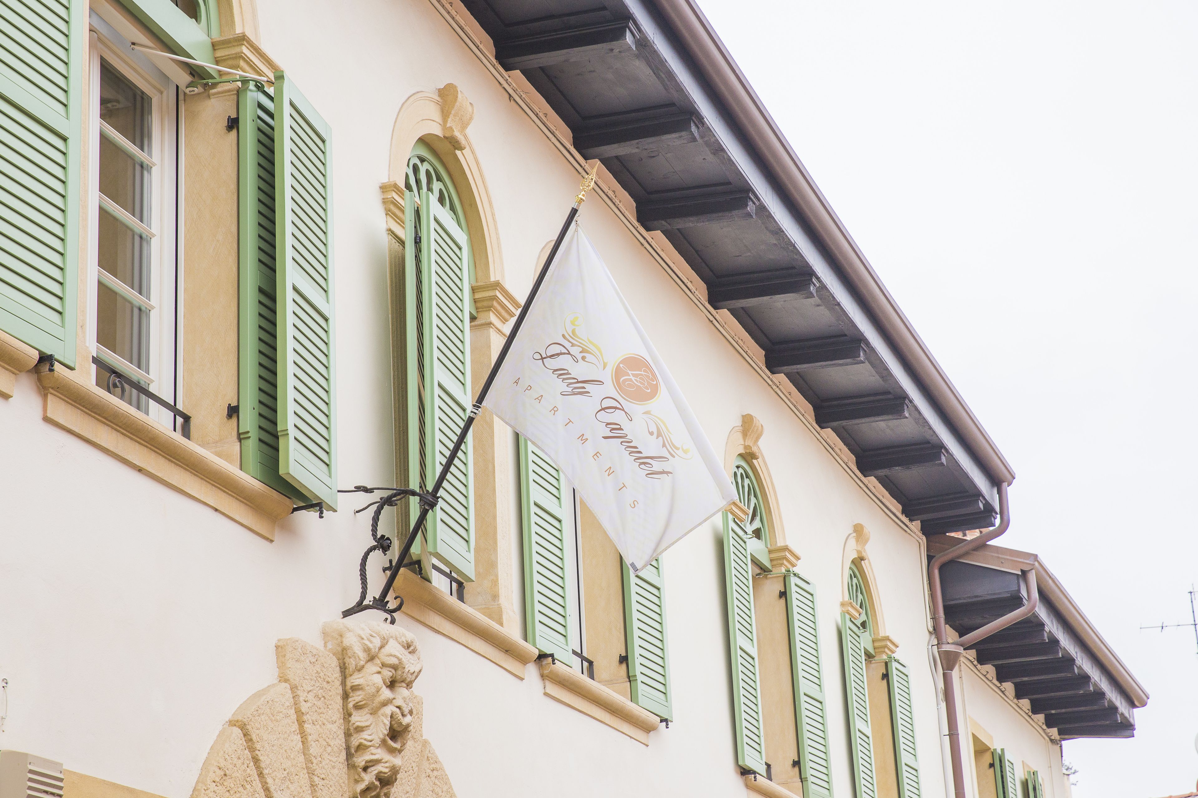 A building with green shutters and a flag reading "Lady Capelle Apartments."