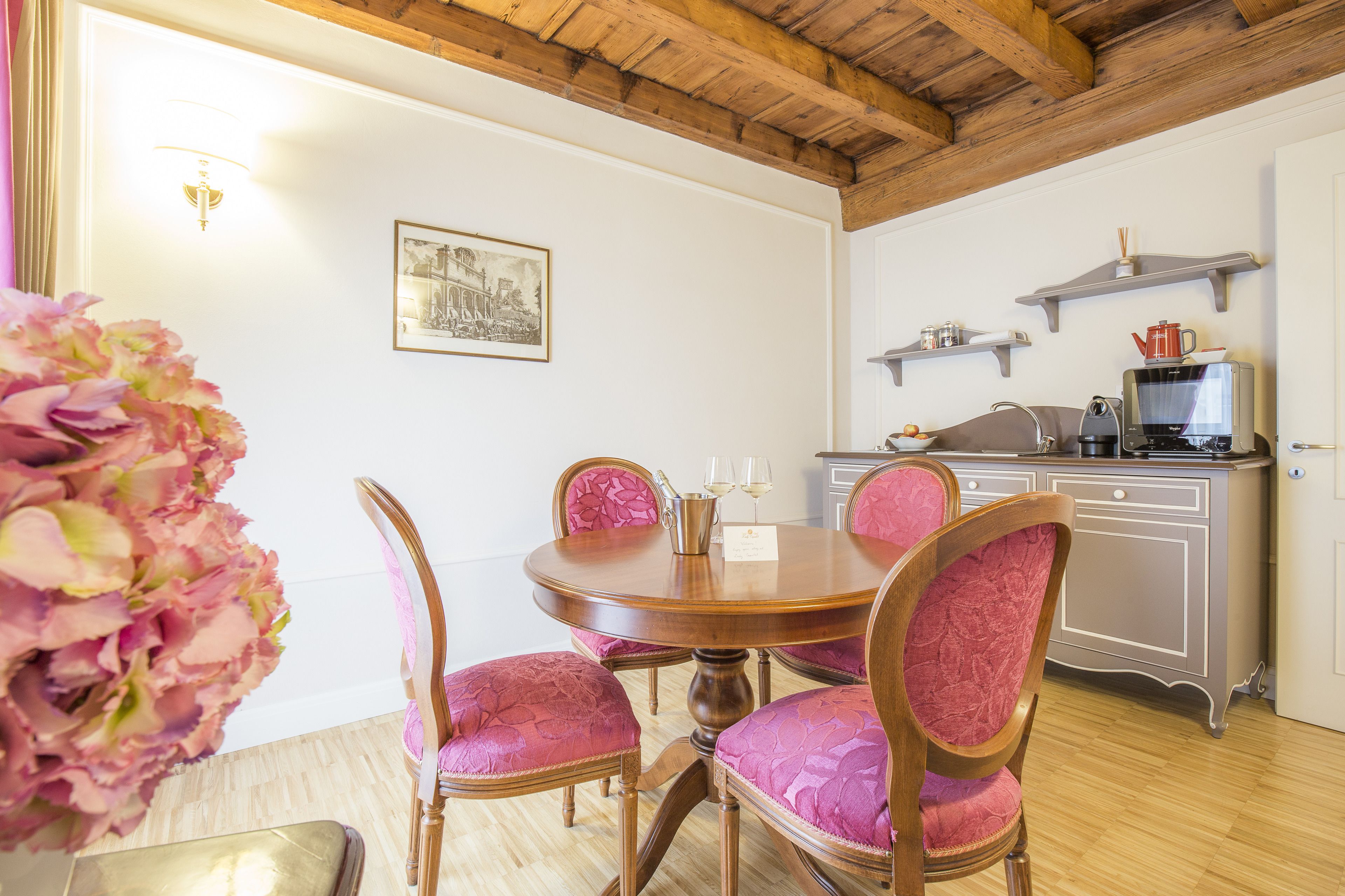 Un coin repas avec une table et des chaises en bois, un vase de fleurs et, au fond, une cuisine.