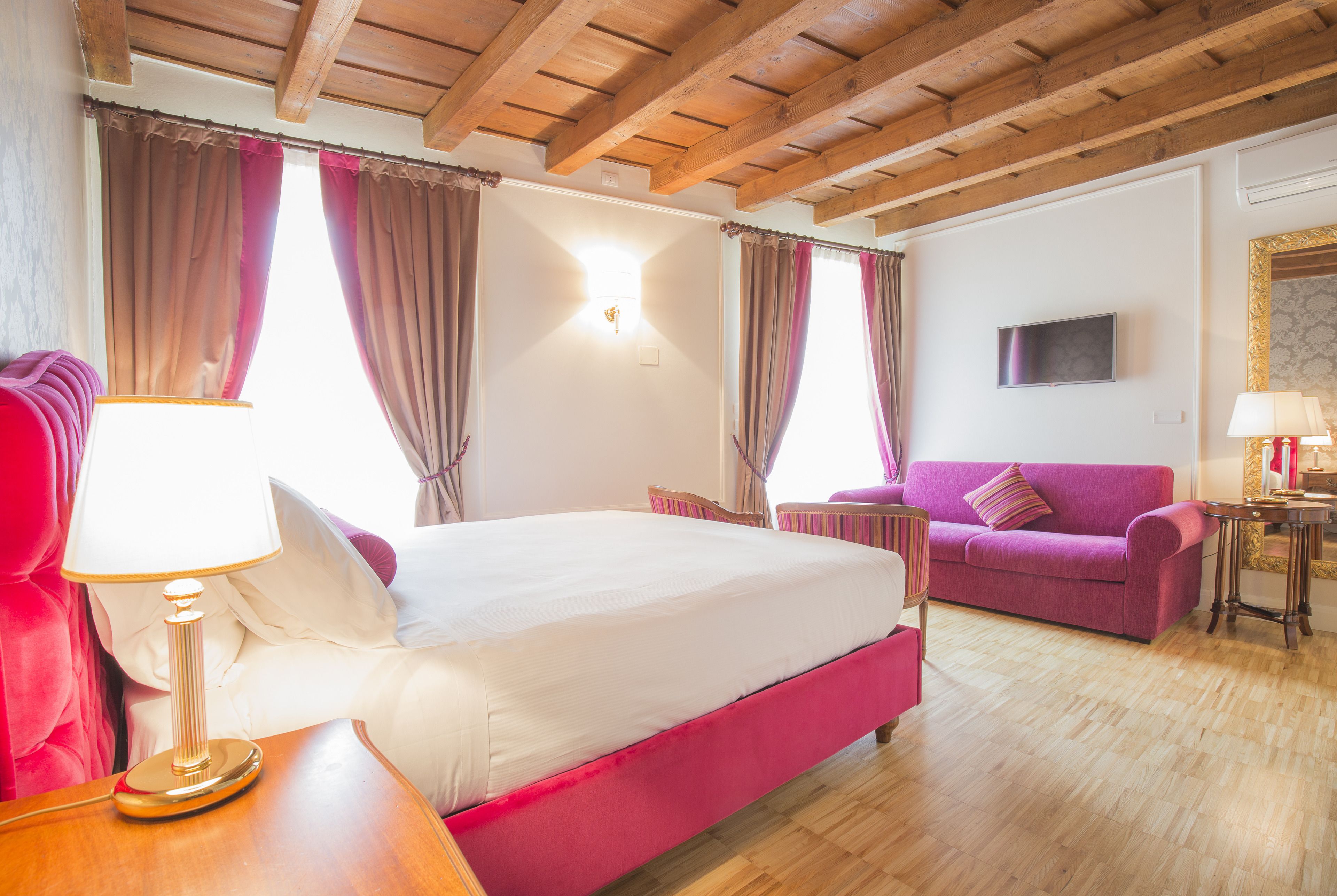 Une chambre avec un grand lit, un canapé rose, une table en bois et un téléviseur fixé au mur.