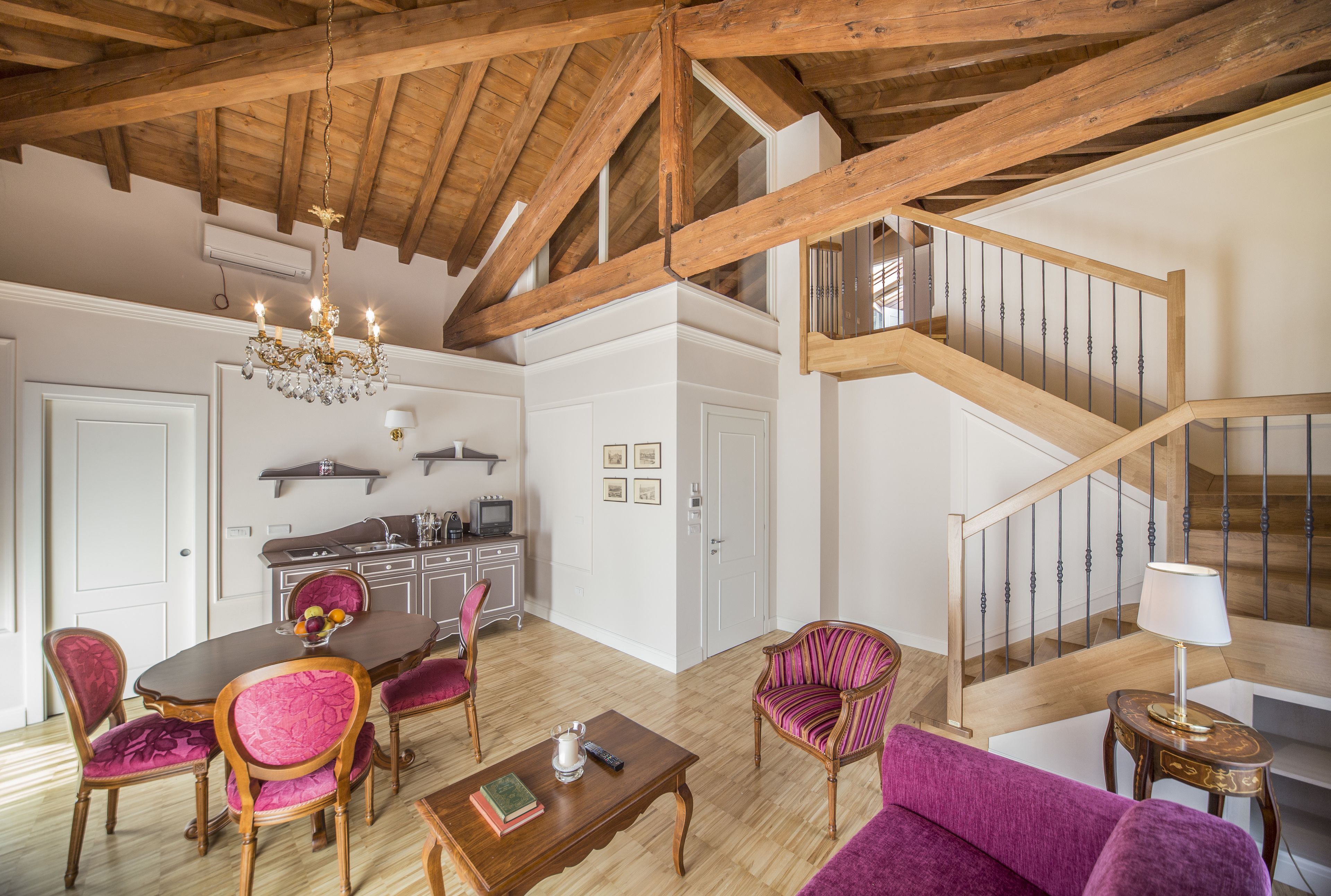 Amplia sala de estar con escalera de madera, una mesa de comedor con sillas y un sofá morado.