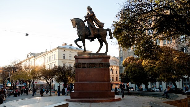 A public square with a statue of a man on a horse, surrounded by trees and buildings.