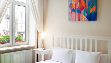 A bedroom with a bed, a nightstand, a lamp, a window with curtains, and a painting on the wall.