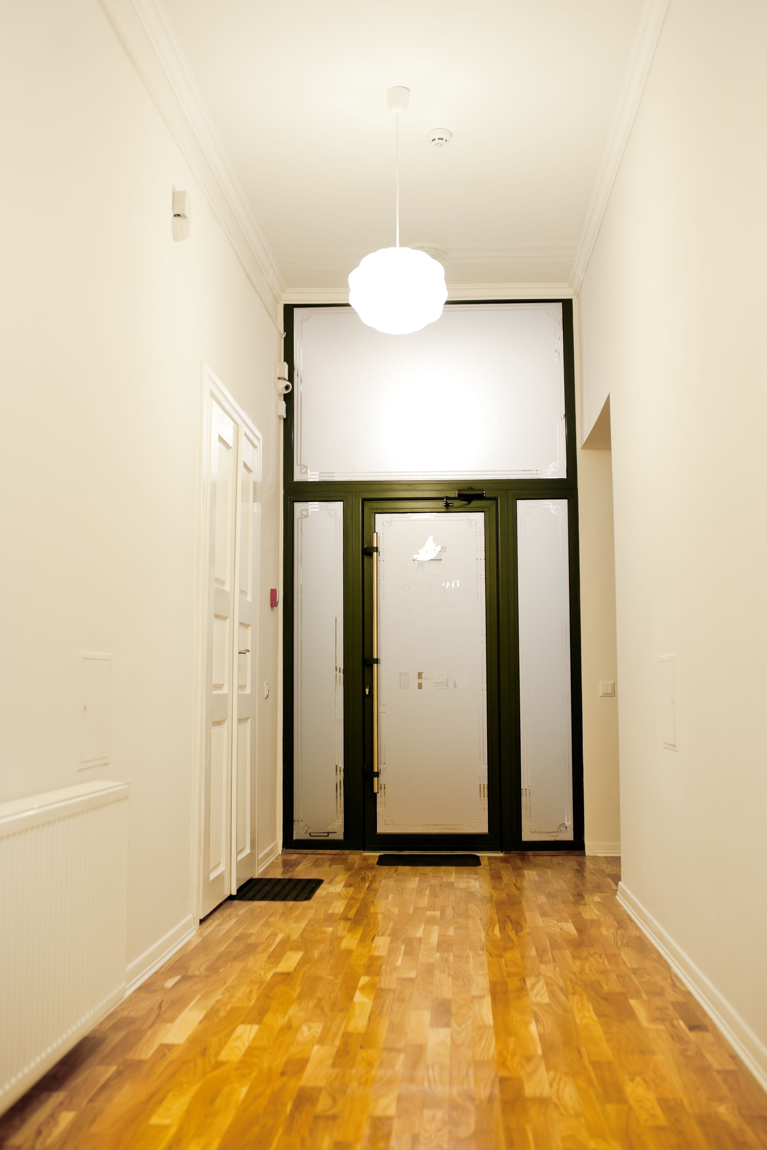 A hallway with wooden flooring, white walls, and a white ceiling light.