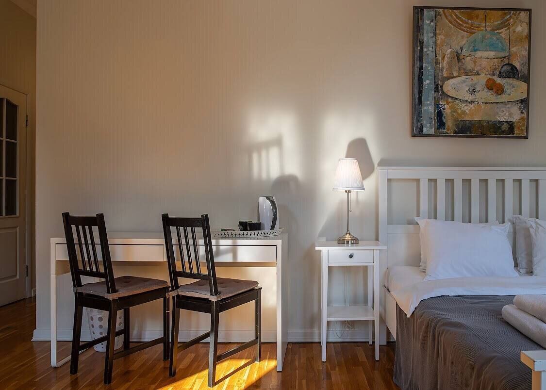 A bedroom with a bed, bedside table, lamp, and two chairs.