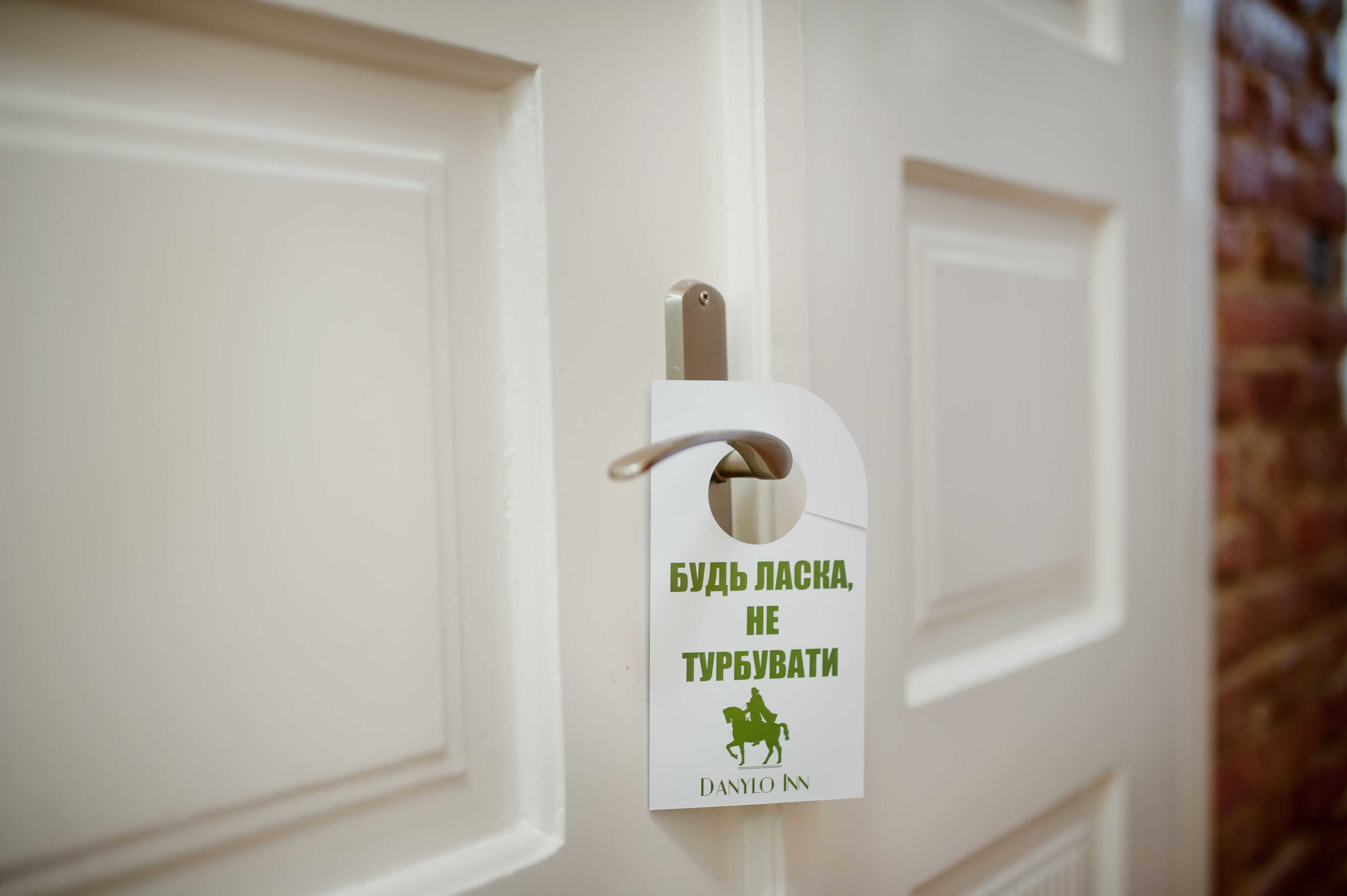 Una puerta con un timbre blanco y un letrero que dice 'БУДЬ ЛАСКА, НЕ ТУРБУВАТИ' y 'DANYLO NN'.