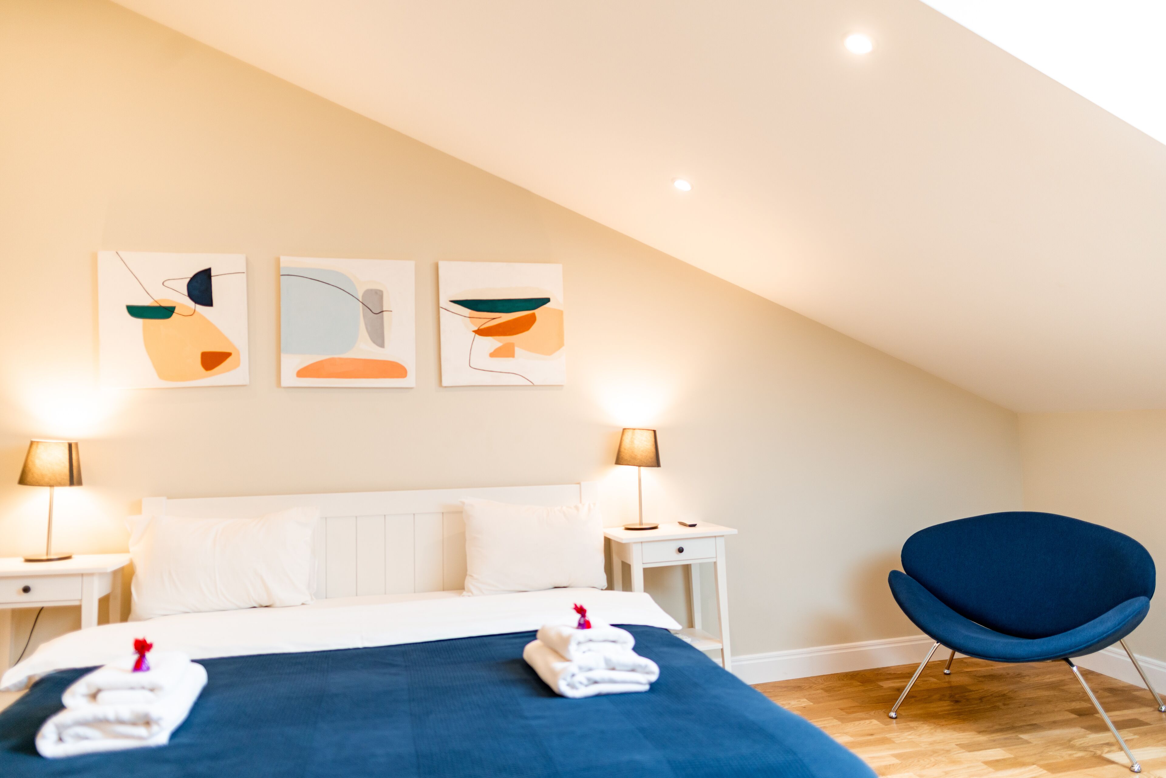 A hotel room with a bed, two bedside tables, a chair, and abstract wall art.
