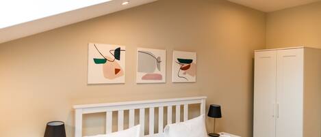 Un dormitorio con cama blanca, mesitas de noche con lámparas, un armario y arte abstracto en la pared.