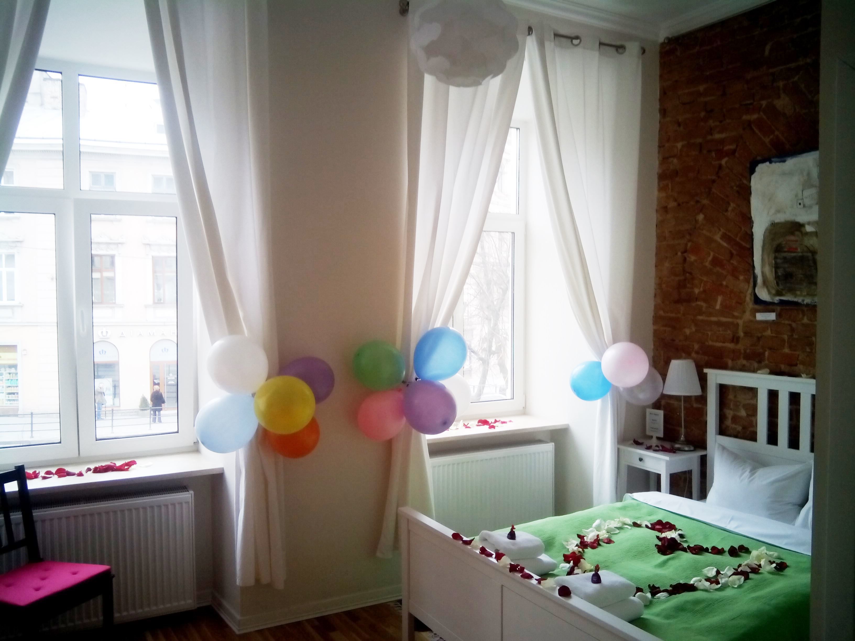 A room with a bed, a chair, a window with curtains, and balloons.