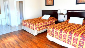 A hotel room with two beds, wooden flooring, and a door leading to a bathroom. - Crossroads Inn & Suites (Victoria)