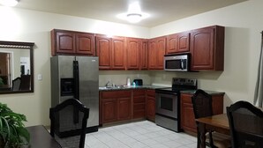 A kitchen with wooden cabinets, a stainless steel refrigerator, a microwave, an oven, and a sink. - Crossroads Inn & Suites (Victoria)