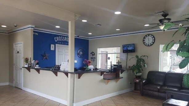 A reception area with a blue wall, a reception desk, a clock, a television, and a leather couch. - Crossroads Inn & Suites (Victoria)