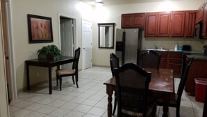A kitchen with wooden cabinets, a refrigerator, a dining table with chairs, and a potted plant. - Crossroads Inn & Suites (Victoria)