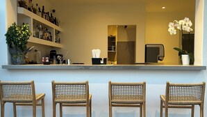 Un rincón de bar con tres sillas de mimbre, una estantería con botellas y una planta en maceta.