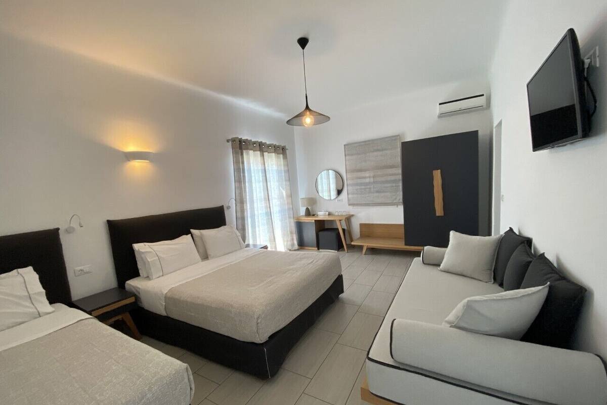 A modern hotel room with a large bed, a sofa, a desk, and a TV.