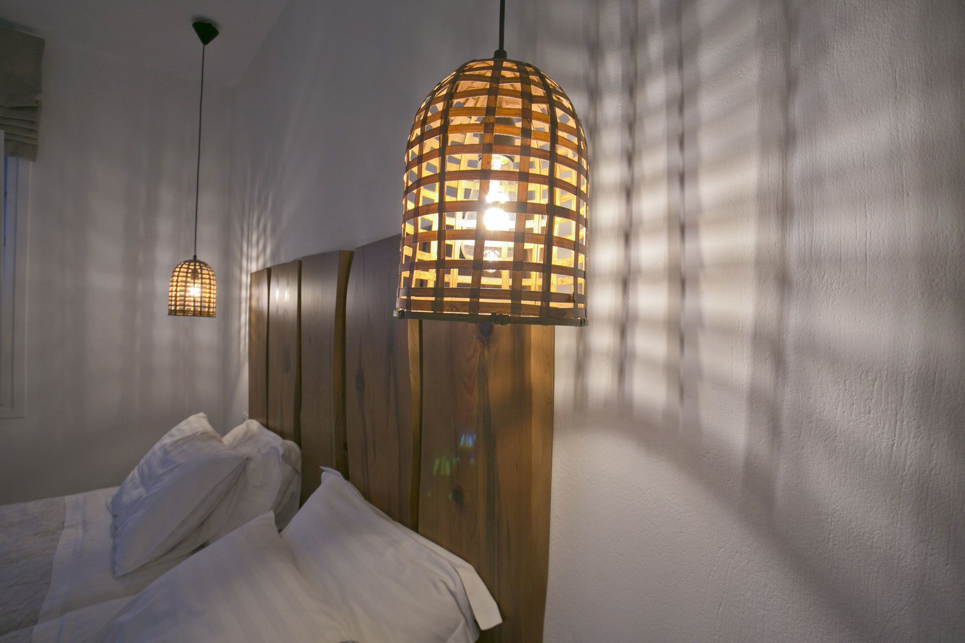 A bedroom with a bed, a wooden headboard, and two hanging pendant lights.
