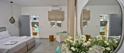 Un dormitorio moderno con un espejo grande, una cama con edredón blanco, una mesita de noche con un jarrón de flores y vista a una piscina a través de la puerta.