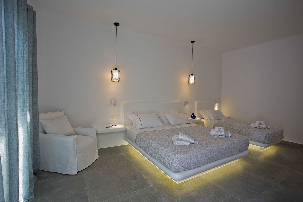 A modern hotel room with two beds, a sitting area, and ambient lighting.