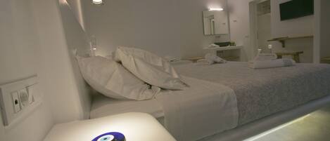 Una habitación de hotel moderna con una cama bien hecha, una mesita de noche con un objeto decorativo y un baño a la vista al fondo.