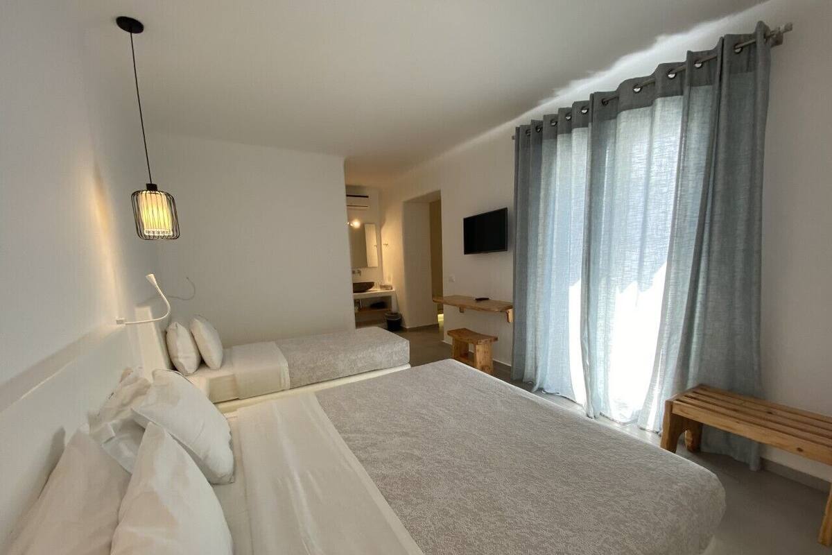 A hotel room with two beds, a wooden bench, a TV, and a window with curtains.