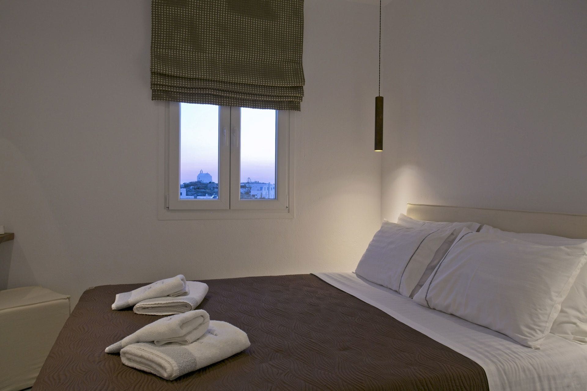 A hotel room with a bed, a window with a view, and a bedside table.
