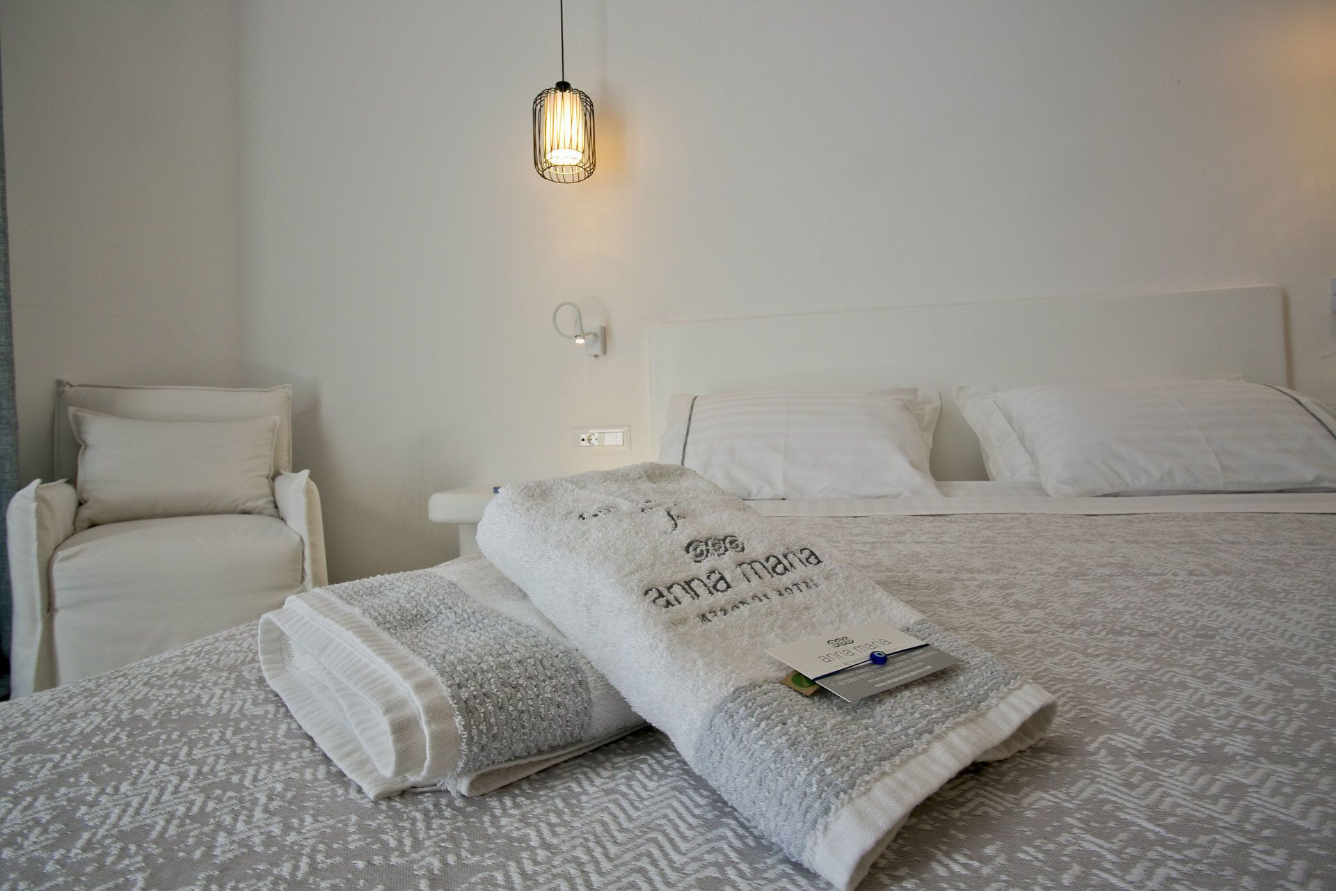Una cama bien hecha con una colcha blanca y dos toallas dobladas.