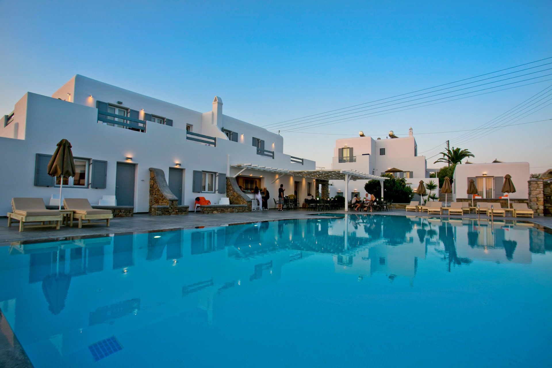 A modern hotel with a pool area, outdoor seating, and a clear blue sky.