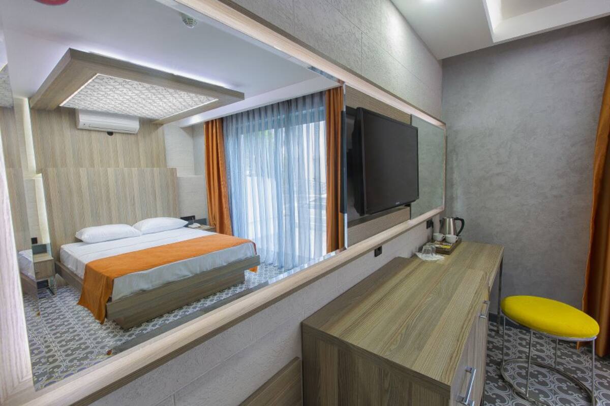 Ein Hotelzimmer mit einem Bett, einem Schreibtisch mit Stuhl, einem Flachbildfernseher und einem Fenster mit Vorhängen.