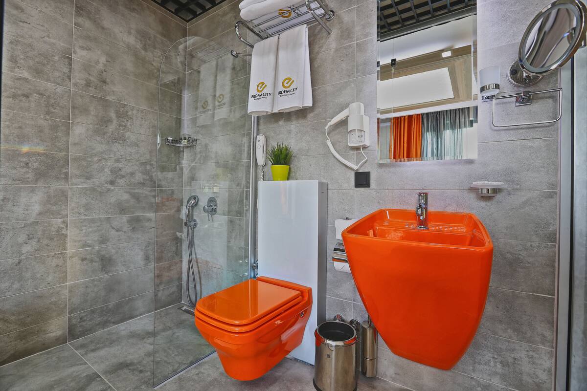 Ein modernes Badezimmer mit einer Duschkabine aus Glas, einer weißen Toilette und einem orangen Waschbecken.