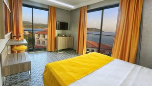 A hotel room with a bed, a desk, a TV, and large windows with curtains. - Erdem City Hotel (Kas)