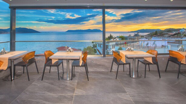 A restaurant with a terrace overlooking a body of water and distant mountains. - Erdem City Hotel (Kas)