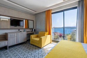 A hotel room with a bed, a sofa, a desk, a chair, a large window with curtains, and a view of the sea. - Erdem City Hotel (Kas)