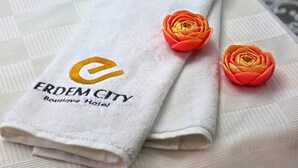 A folded white towel with the text "ERDEM CITY Boutique Hotel" and two artificial red roses. - Erdem City Hotel (Kas)