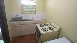 A small kitchen with a gas stove, a sink, and a window with bars. - Moon Rooms at Moonrise Villa (Negril)